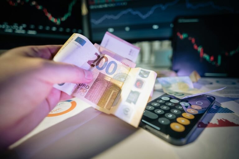 A hand holds euro notes with financial charts and a calculator, symbolizing investment and trading.