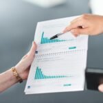 Two people analyzing a document with green bar charts